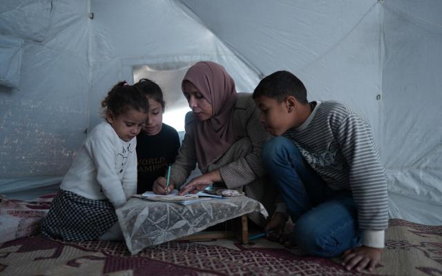 Hiba and her children in her tent in Al Mawasi. She is teaching them.